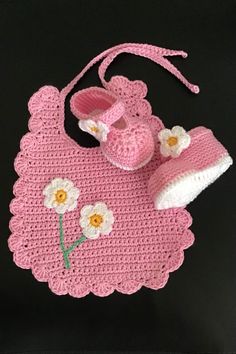 a pink crocheted baby's outfit and booties on a black background