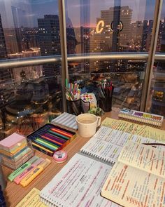 an office desk with lots of papers and pencils on it, in front of a large window overlooking the city