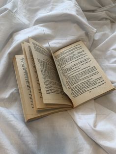 an open book sitting on top of a bed next to a white comforter covered in sheets