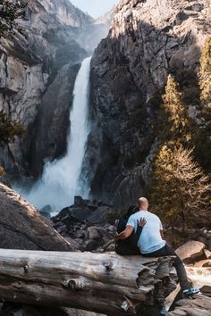 a man sitting on a log looking at a waterfall