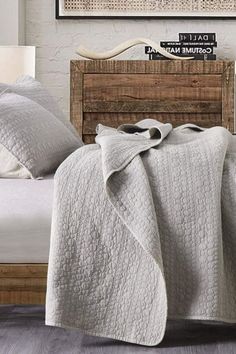 a bed with a blanket on top of it next to a wooden headboard and night stand