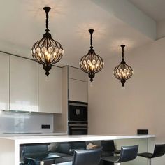 three chandeliers hanging from the ceiling above a kitchen island with bar stools