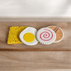 two decorated cookies sitting on top of a wooden tray next to a cupcake and sauce