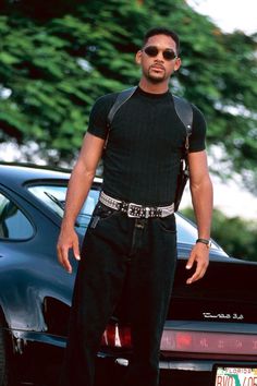 a man standing in front of a car with sunglasses on his head and wearing black pants