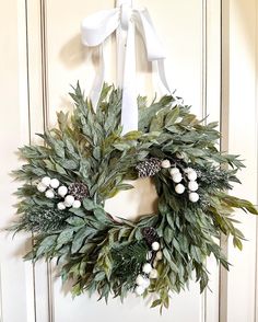 a wreath with white berries and greenery hanging on a door