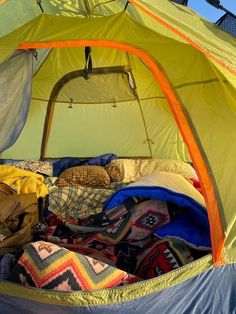 the inside of a tent with blankets, pillows and other items in it that is open