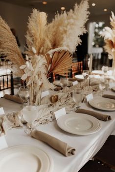 the table is set with white plates and silverware, pamodia in vases