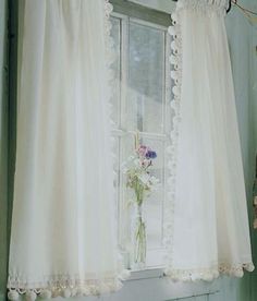 a white curtain hanging in front of a window next to a vase filled with flowers