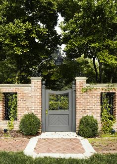 an entrance to a brick house with a gate and two bushes in the foreground