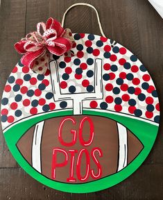 a painted football sign with the word go pos on it and a bow hanging from its center