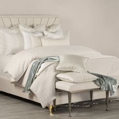 a bed with white linens and pillows on the headboard, in a bedroom