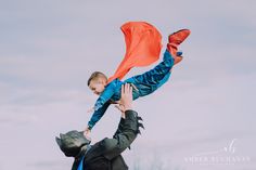 a man holding a child up in the air with an orange scarf on his back