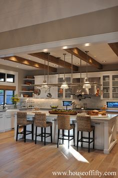 a large kitchen with white cabinets and wooden floors is pictured in this image, there are four stools at the center of the island