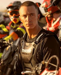 a man standing next to a group of motorcyclists in black and red gear