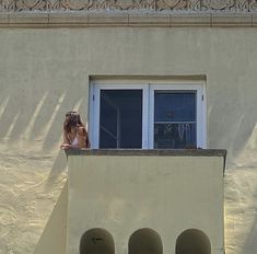 a woman standing on top of a balcony next to a window with her hair blowing in the wind