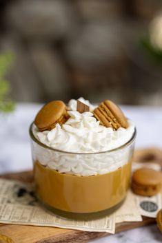 a dessert in a glass bowl with whipped cream and cookies on the side, sitting on top of a wooden cutting board