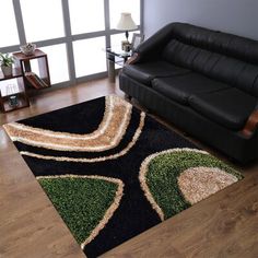 a living room with a black leather couch and green rugs on the wooden floor