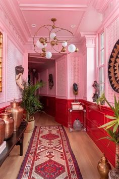 a hallway with pink walls and rugs, potted plants and vases on the floor