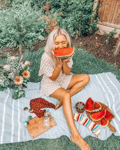 a woman sitting on the grass eating a piece of watermelon