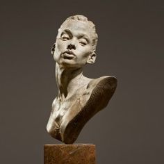 a statue of a man's head on top of a marble block in front of a gray background