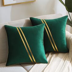 two green and gold striped pillows on a white couch next to a potted plant