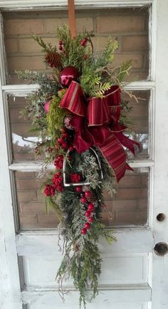 a christmas wreath hanging on the front door with red bows and evergreens in it