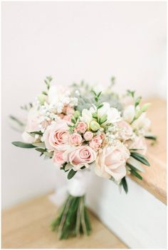 a bouquet of pink and white flowers sitting on top of a wooden table next to a mirror