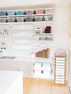 an organized craft room with white shelving and lots of storage containers on the wall