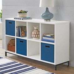 a white and blue bookcase with three bins on top of it next to a lamp