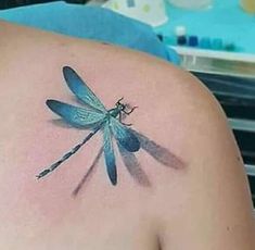 a blue dragonfly tattoo on the back of a woman's shoulder