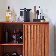 a wooden cabinet with bottles and other items on it's shelf, in front of a white wall