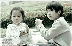 two young children sitting next to each other in front of a bush and grass area