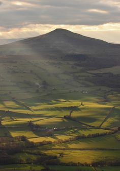 the sun shines brightly through the clouds over rolling hills and fields on a cloudy day