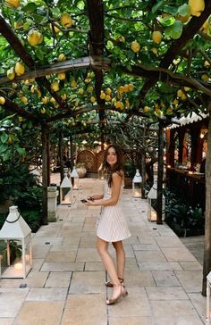 a woman in a white dress is standing under a tree with lemons on it