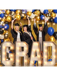 three people in graduation caps and gowns posing for a photo with the word grad surrounded by balloons