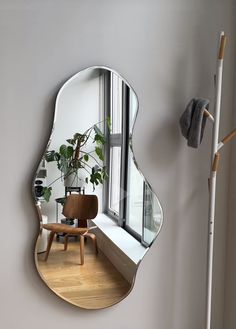 a mirror that is on the side of a wall next to a chair and potted plant