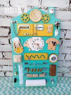 a blue and yellow clock with various items on it's face, attached to a brick wall