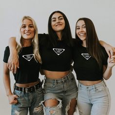 three young women standing next to each other in front of a white wall wearing black t - shirts