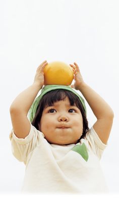 a young child holding an orange on top of his head