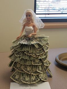 a barbie doll dressed in a wedding dress made out of dollar bills on top of a table