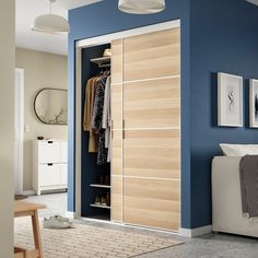 an open closet with clothes hanging on the wall, and a bed in the foreground