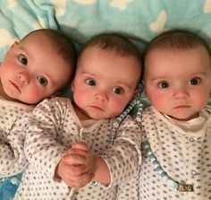 three baby babies laying next to each other on a blue and white bedspread