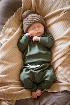 a baby is sleeping on a bed wearing a knitted hat and green jumpsuit