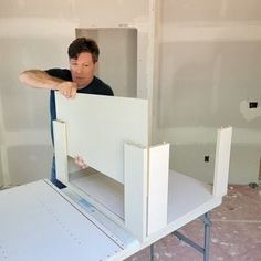 a man standing in front of a white table with two pieces of furniture on it