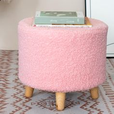 a pink ottoman with wooden legs and a book on top