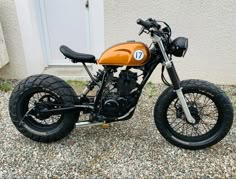 an orange and black motorcycle parked in front of a white building with gravel on the ground