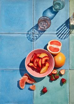 a bowl of fruit sitting on top of a blue tiled floor next to two glasses