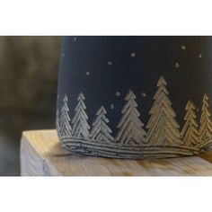 a cup that is sitting on top of a wooden block with trees painted on it