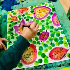 a child's hand is drawing leaves on a piece of paper