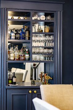 a blue cabinet filled with lots of bottles and glasses next to a dining room table